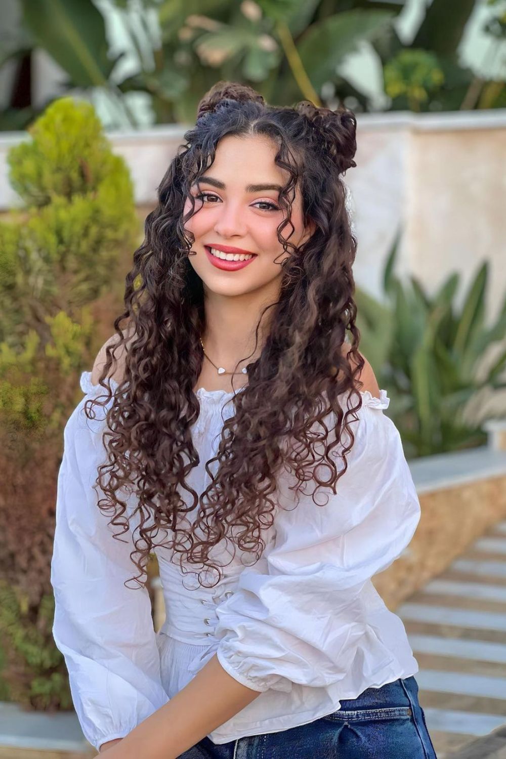 A woman with long curly hair and with half-up half-down hairstyle.