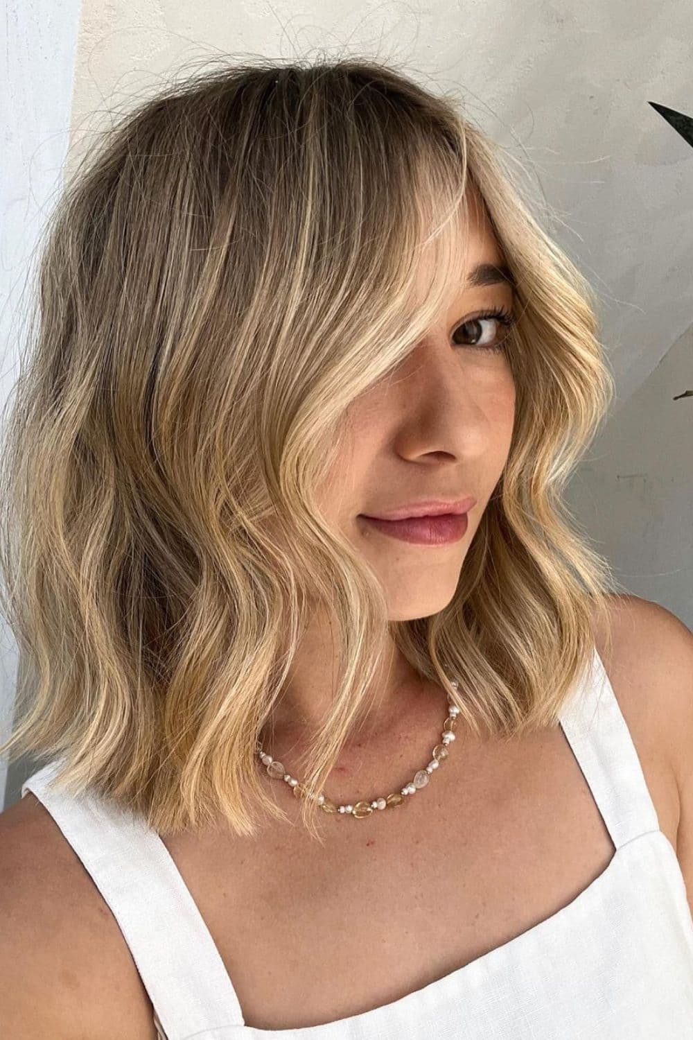 A woman with a blonde face-framing highlights and beach waves.