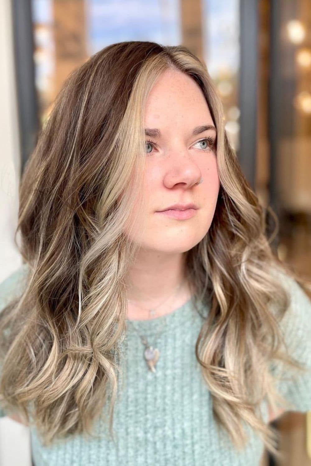 A woman with long bronde center part hair with blonde money pieces.