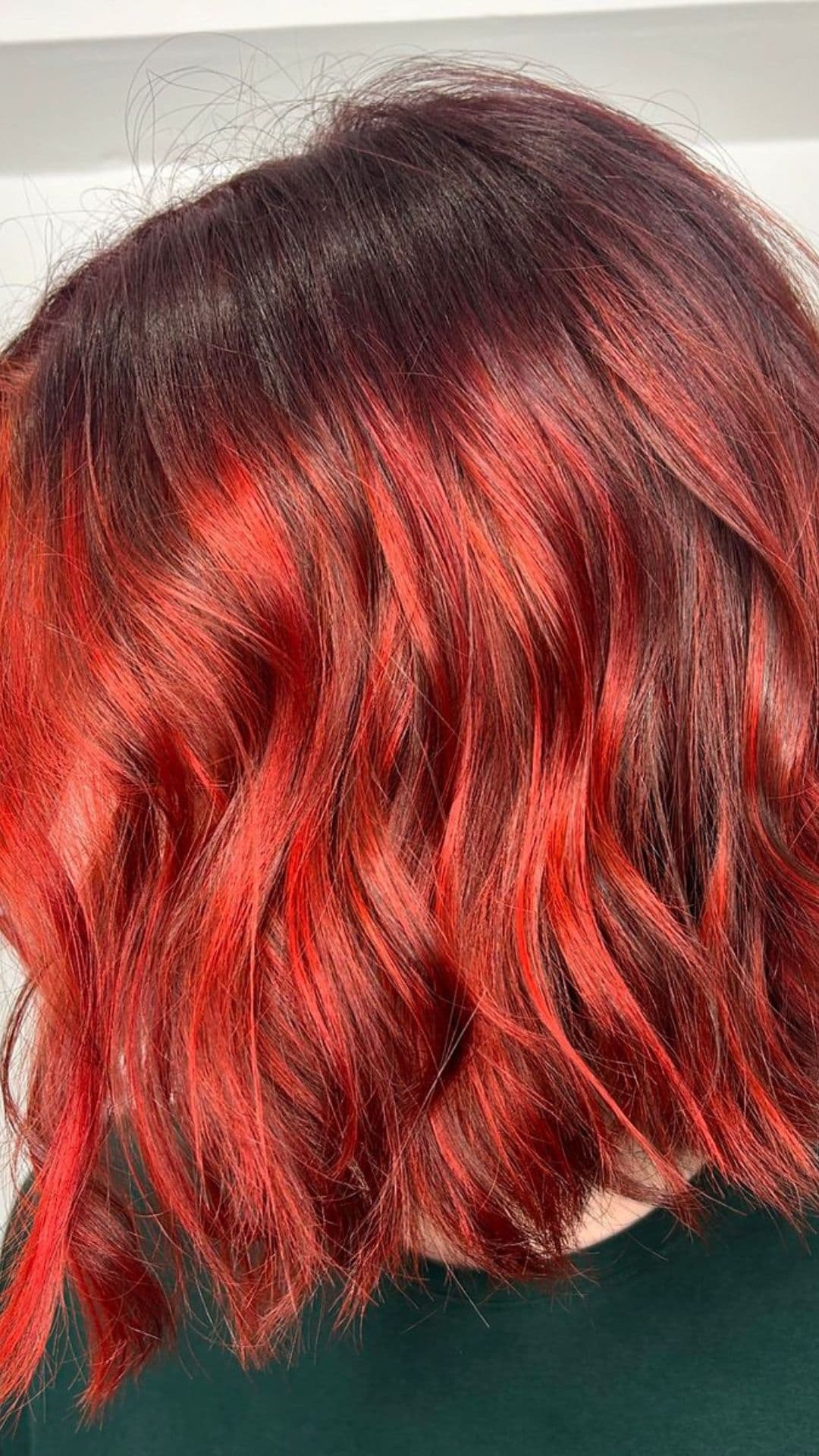 A person models a Fireplace Flame Ombre hairstyle, featuring rich red and orange tones transitioning into darker roots.