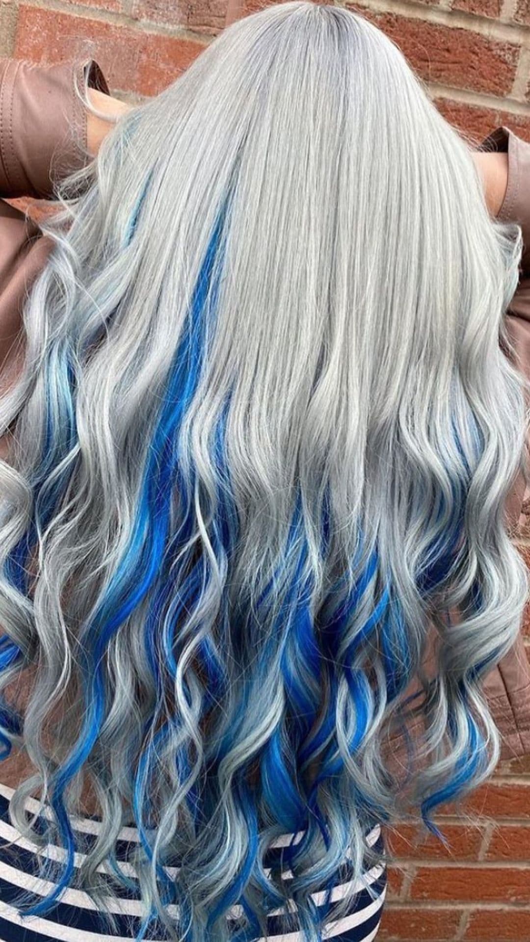 Silver and sapphire hairstyle with long, wavy hair featuring vibrant blue streaks. The person is turned away, showcasing the hair's texture and color.