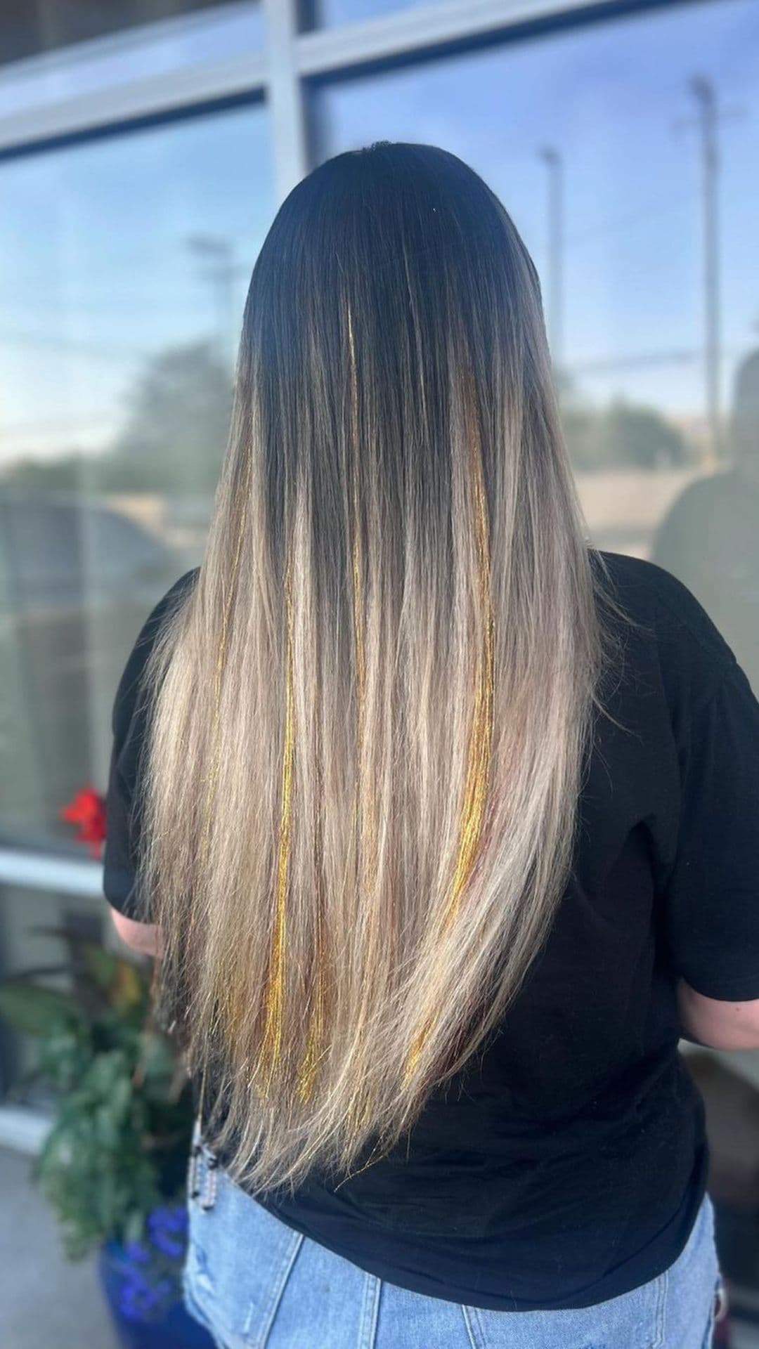 A person with long, straight hair showcasing Tinsel Highlights against an outdoor background.