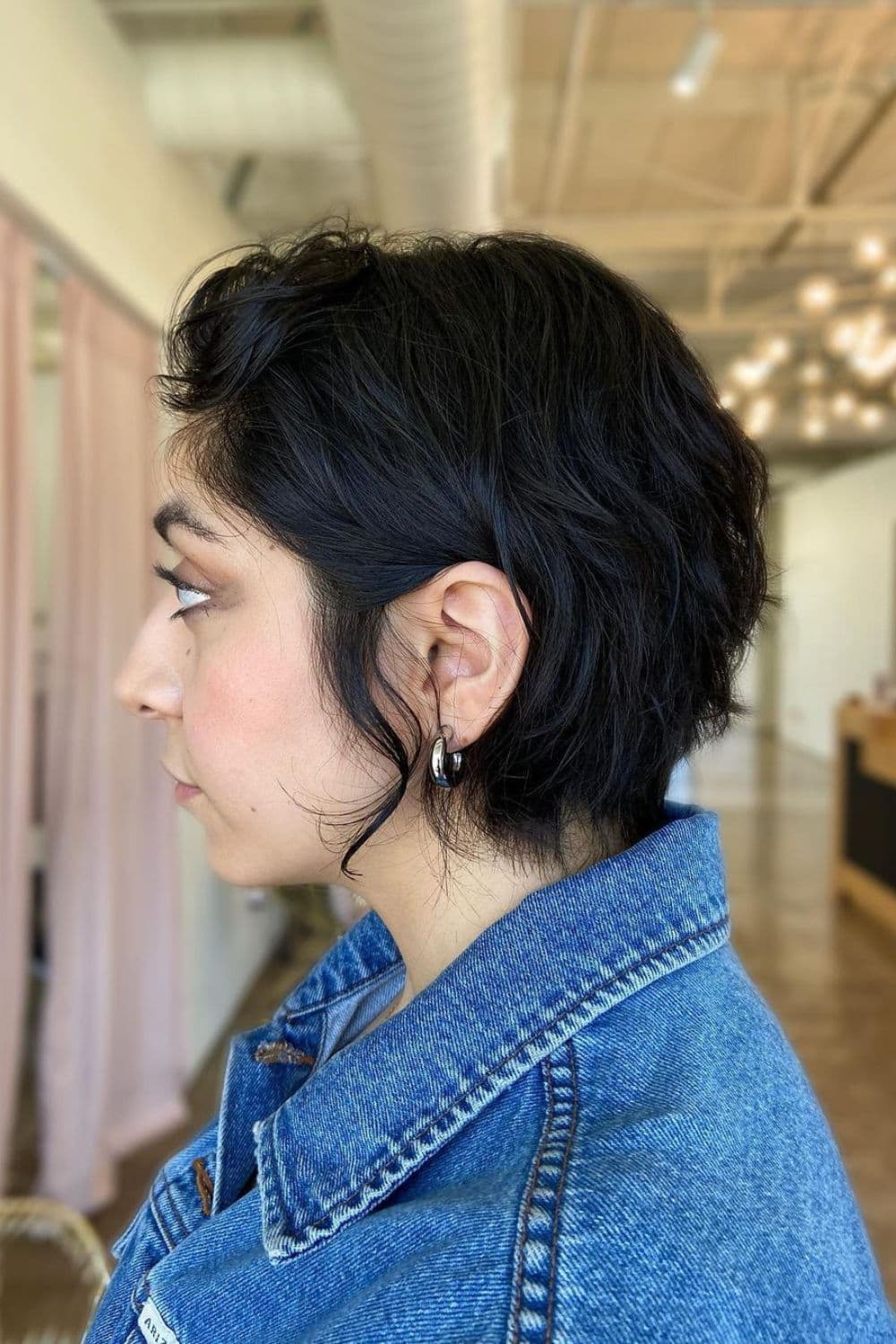 Side view of a woman wearing a denim jacket with classic wavy bixie hair.