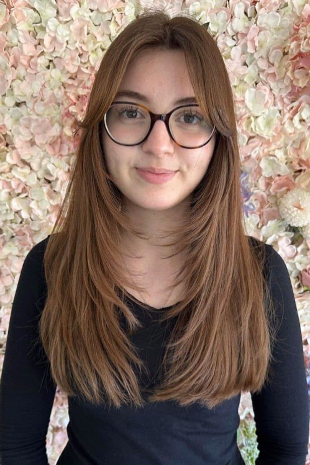 A woman wearing eyeglasses with long brown feathered layers.