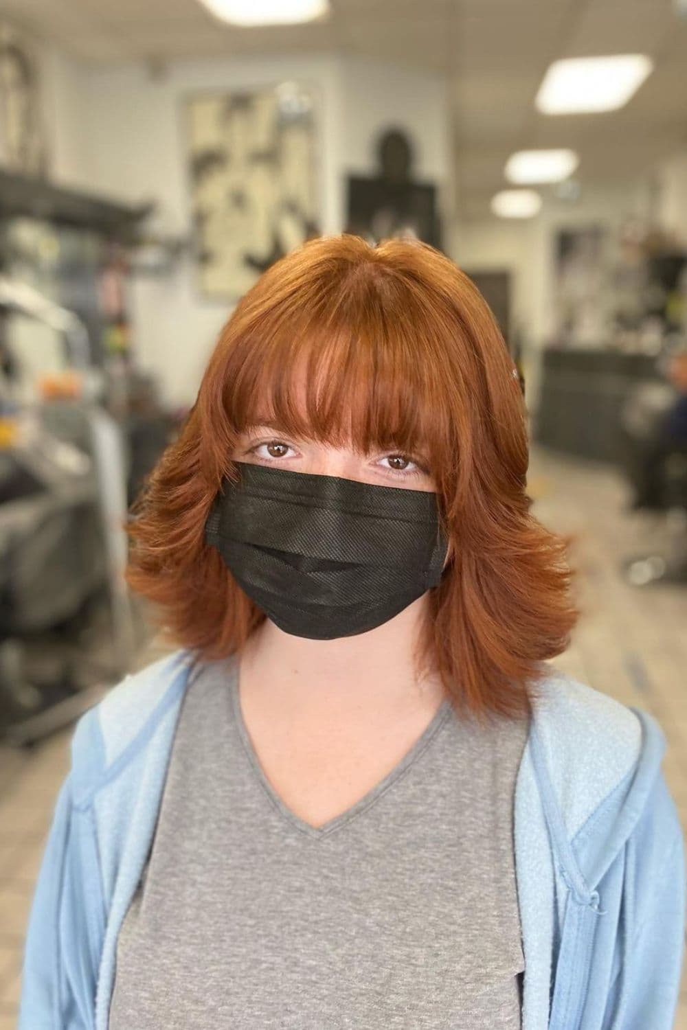 A woman wearing a black face mask with a light brown flipped-up feathered cut.