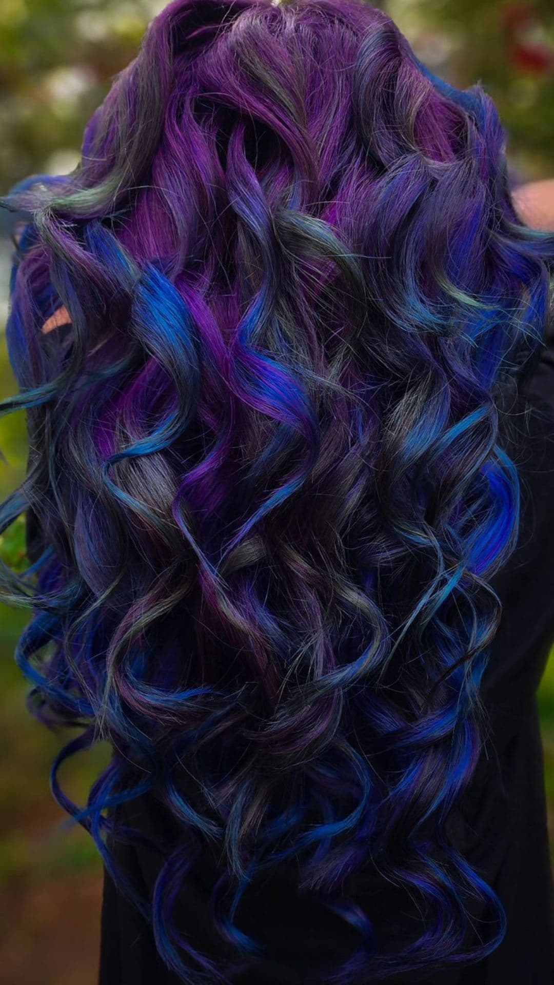 Curly hair dyed in Deep Sea Indigo, featuring rich purple and blue tones. Fashionable and vibrant.