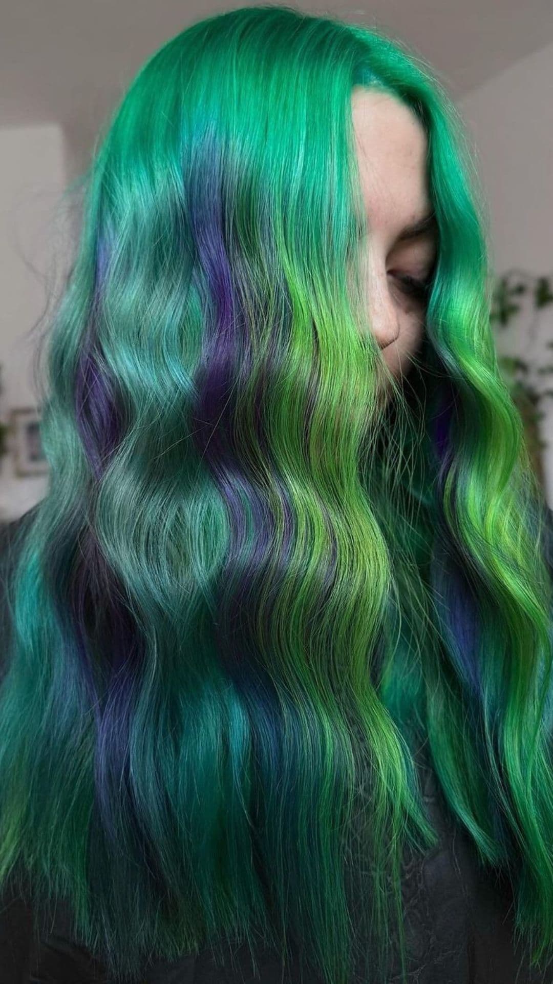 Person with wavy, vibrant green and blue hair modeling the Enchanted Evergreen hairstyle.