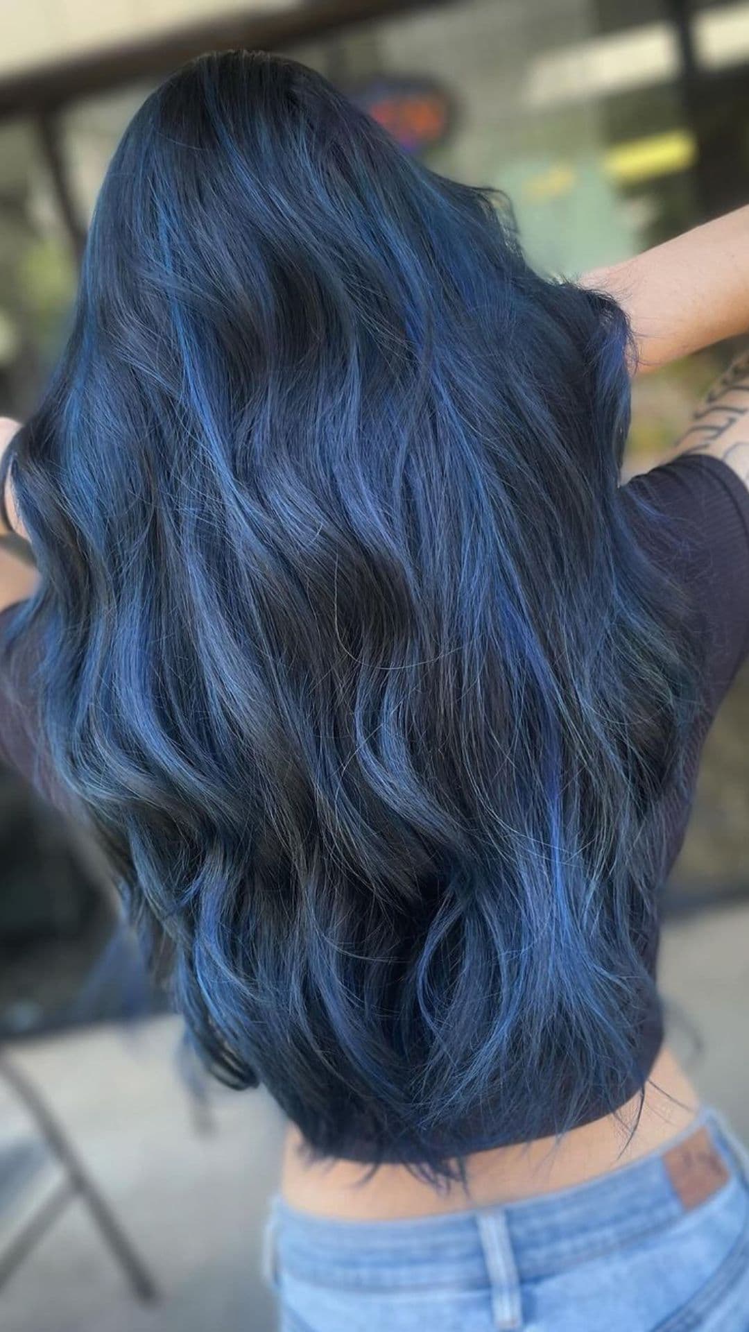 Person showing off long, wavy Oceanic Midnight Blue hairstyle from the back, wearing a black top and jeans.