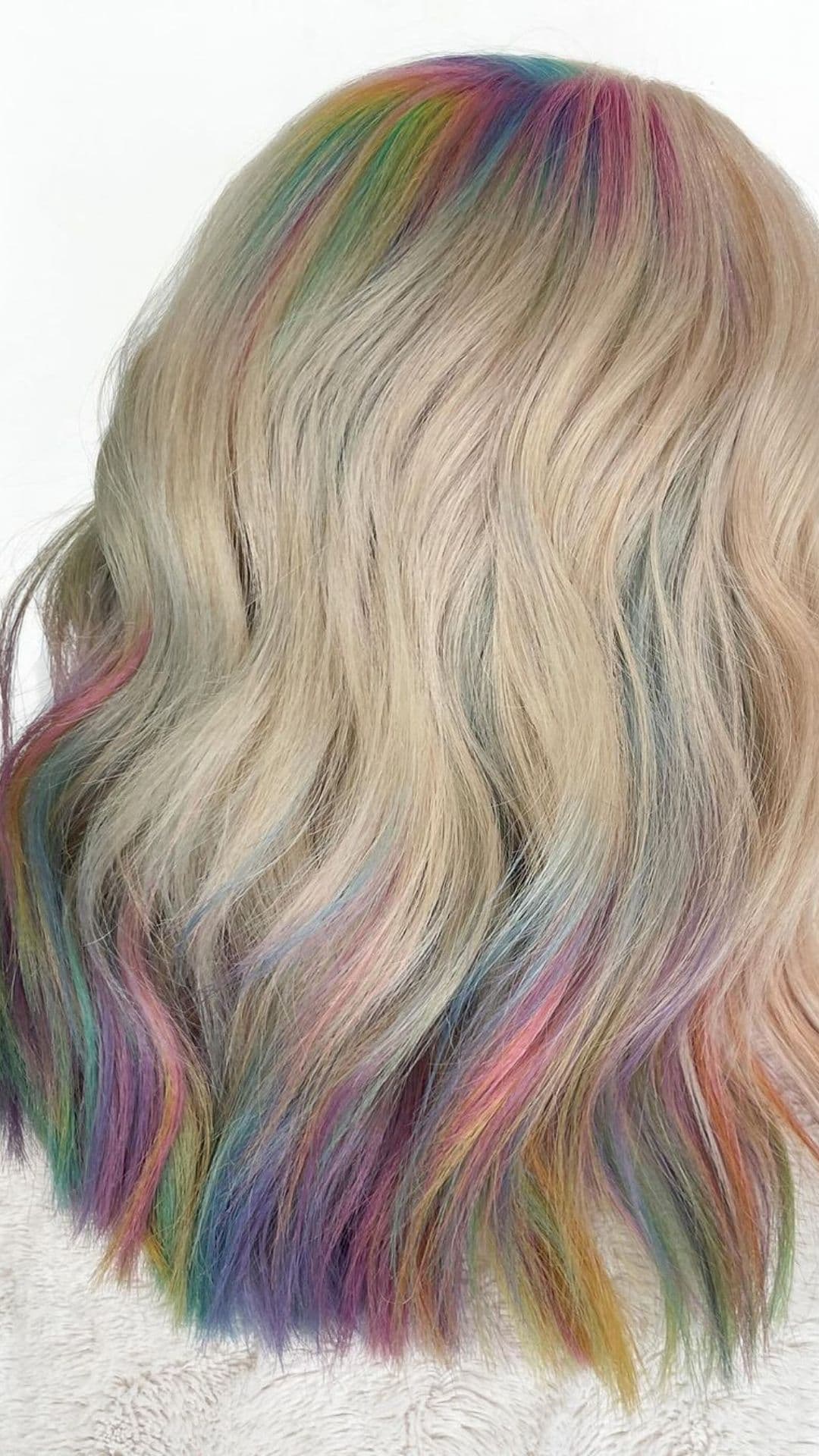 Back view of a person modeling a Sandy Blonde hairstyle with Mermaid Hues, featuring soft waves and colorful highlights in pink, blue, and green.