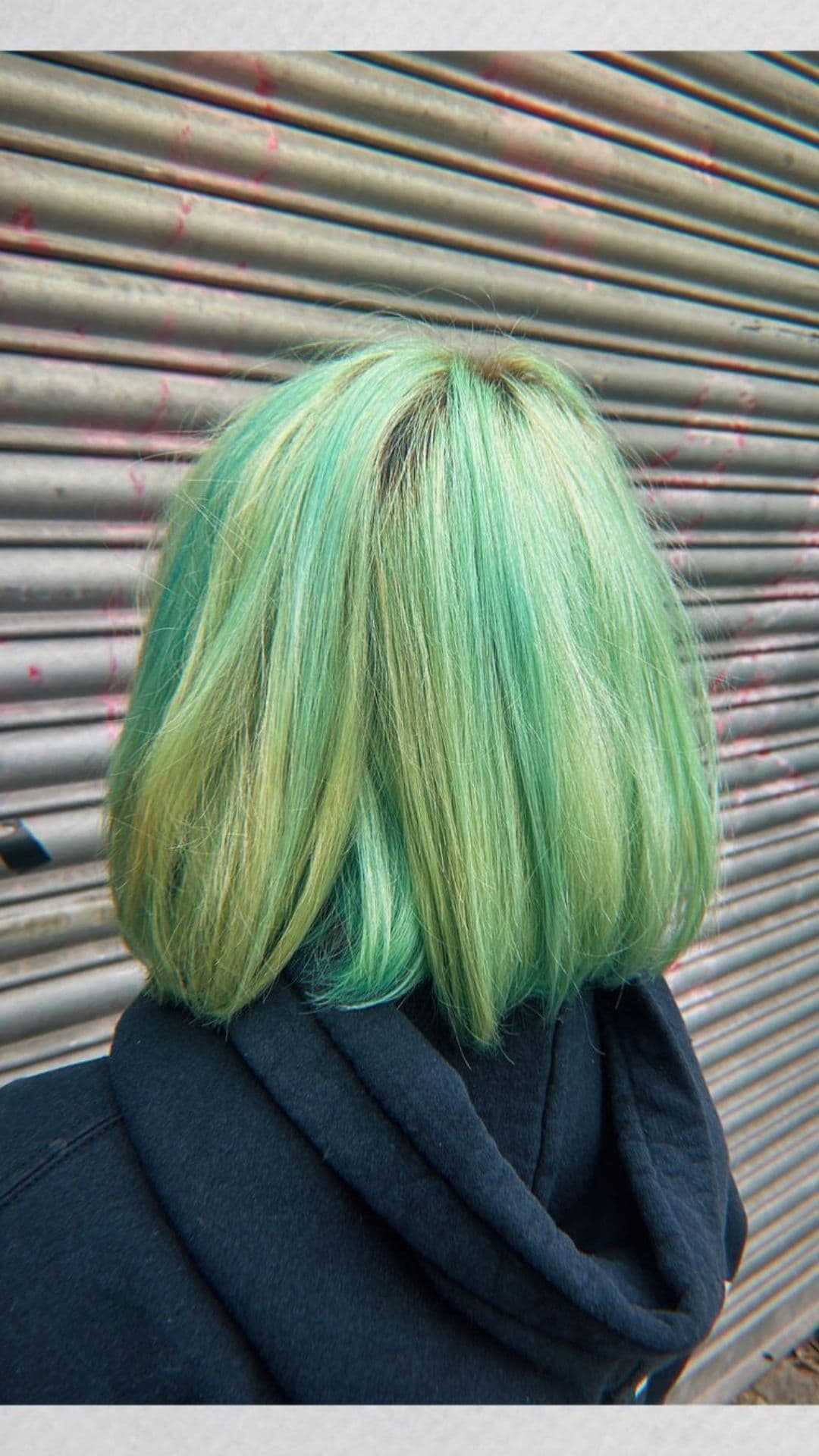 Person with a Seafoam Green Balayage hairstyle facing a metal shutter background.