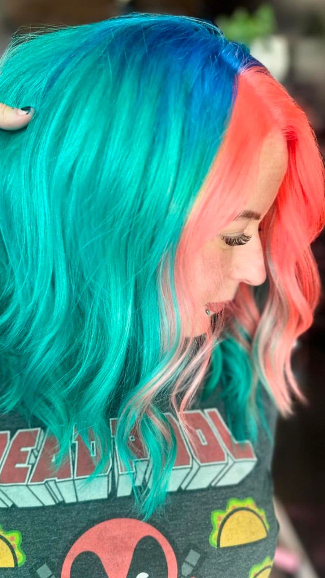 A person models the Serene Coral Sunset hairstyle, featuring vibrant teal and coral colors.