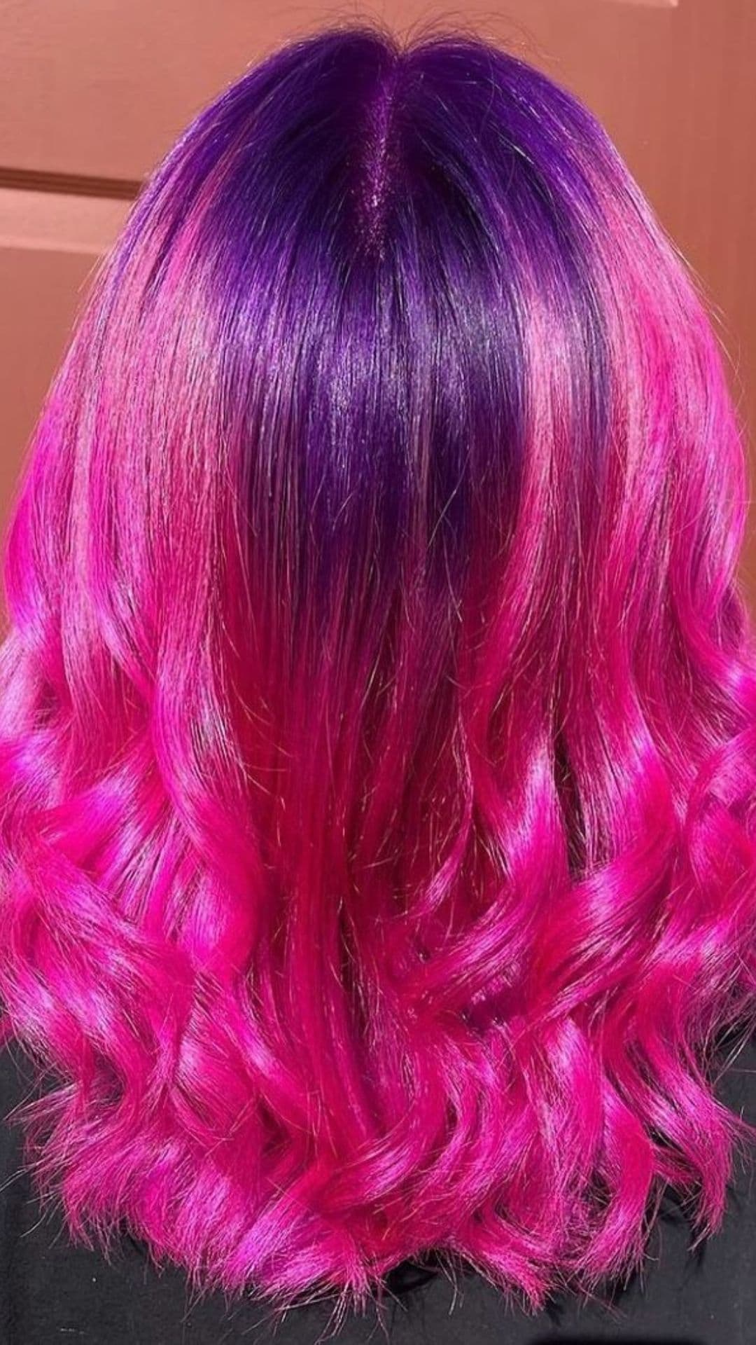 A model showcases a hairstyle with sunset pink and purple tones, featuring loose waves.