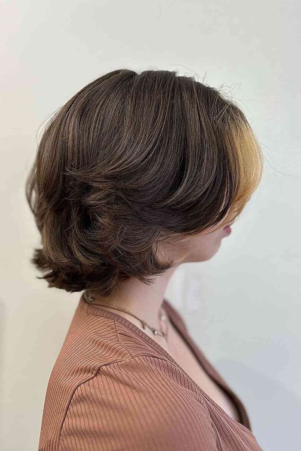 Side view of a woman with a short brown wolf cut with a blonde highlight in front.