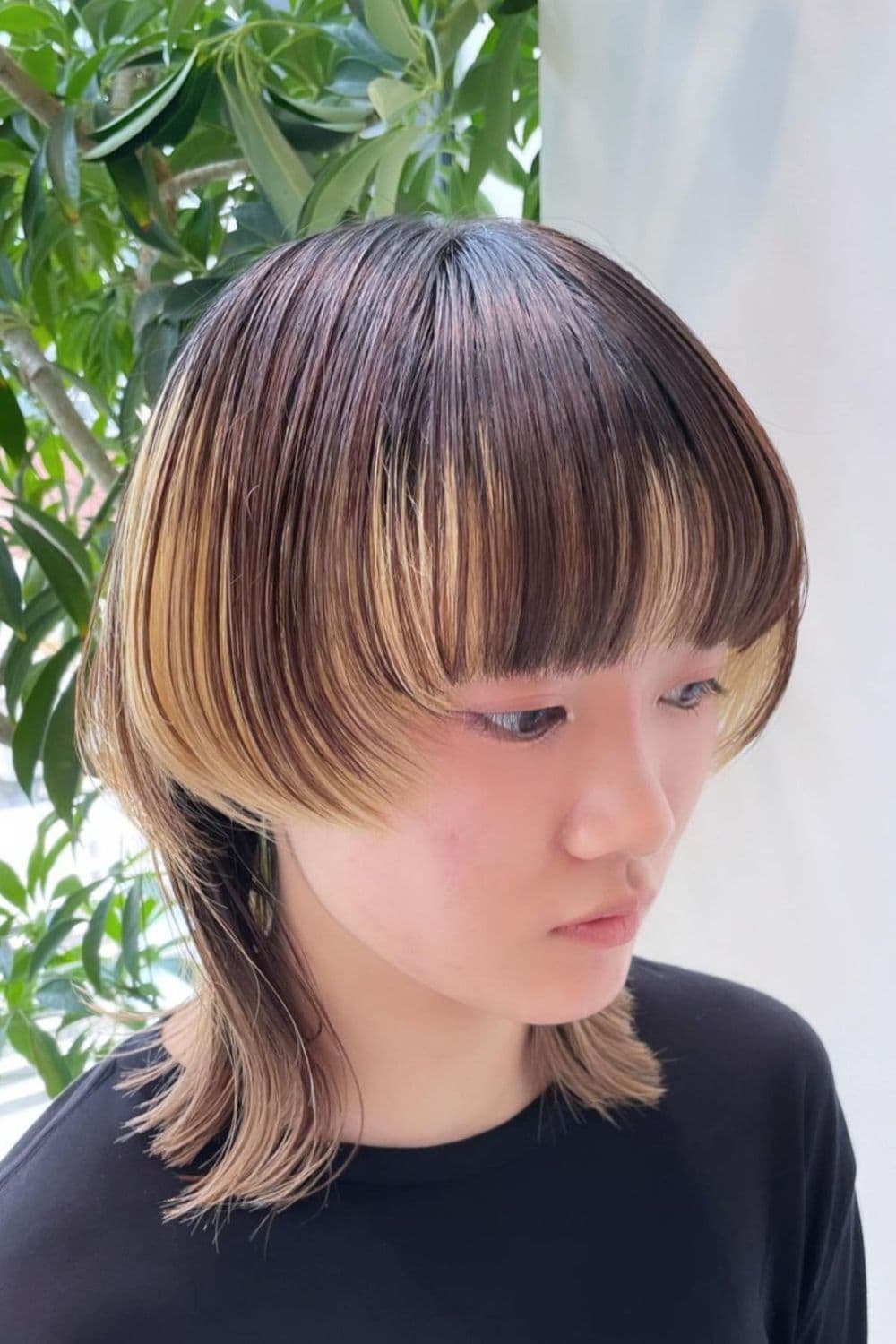 A woman with a black and blonde short wolf cut with heavy bangs.