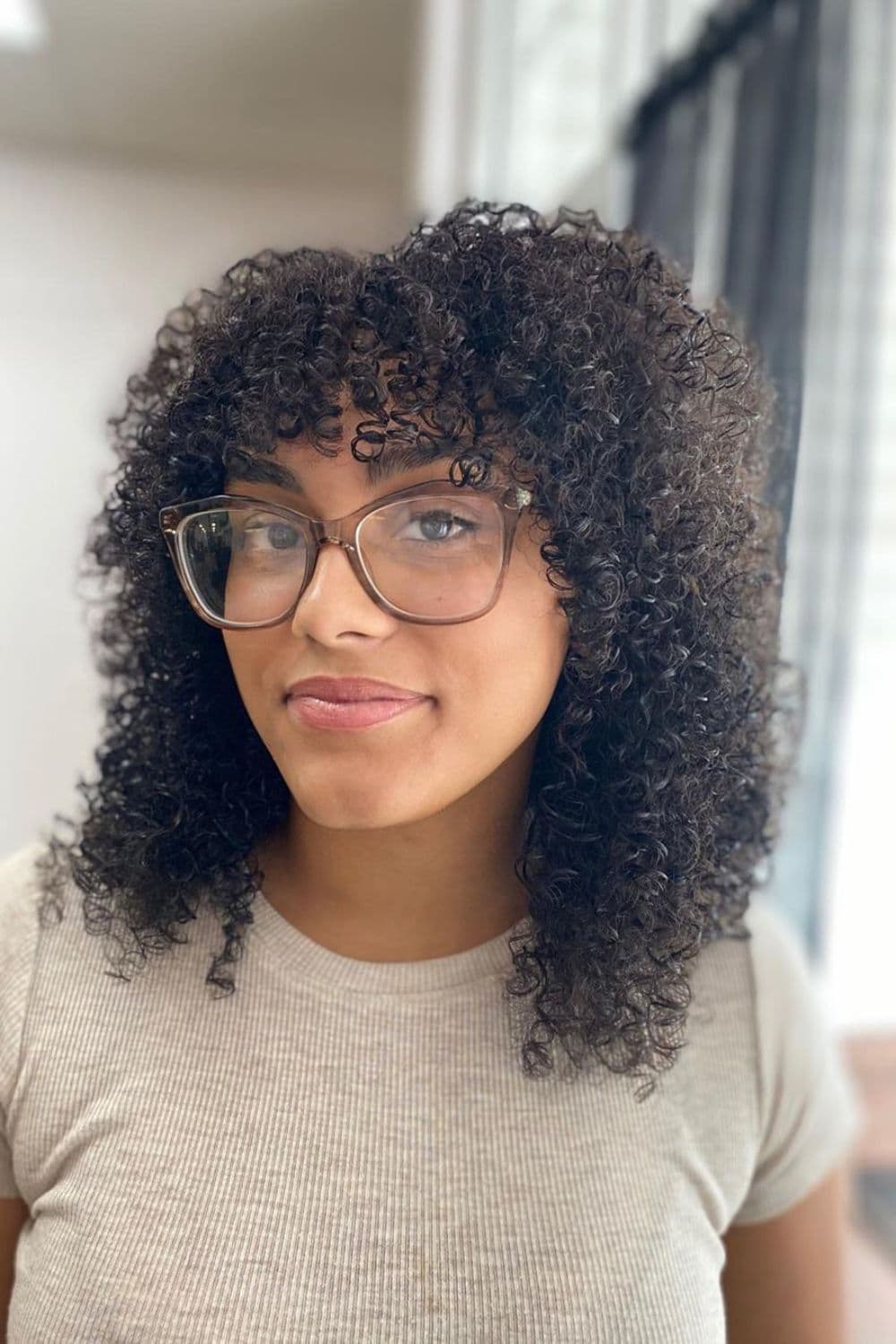 A woman wearing eyeglasses with black shoulder-length curly layers.