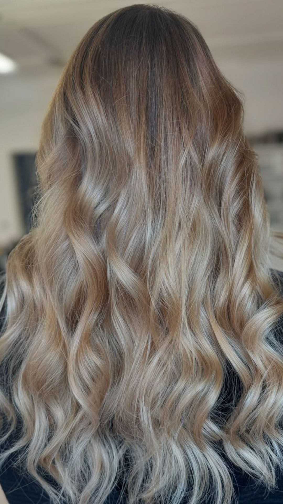 Back view of a person modeling a Champagne Blonde hairstyle with soft, natural waves.