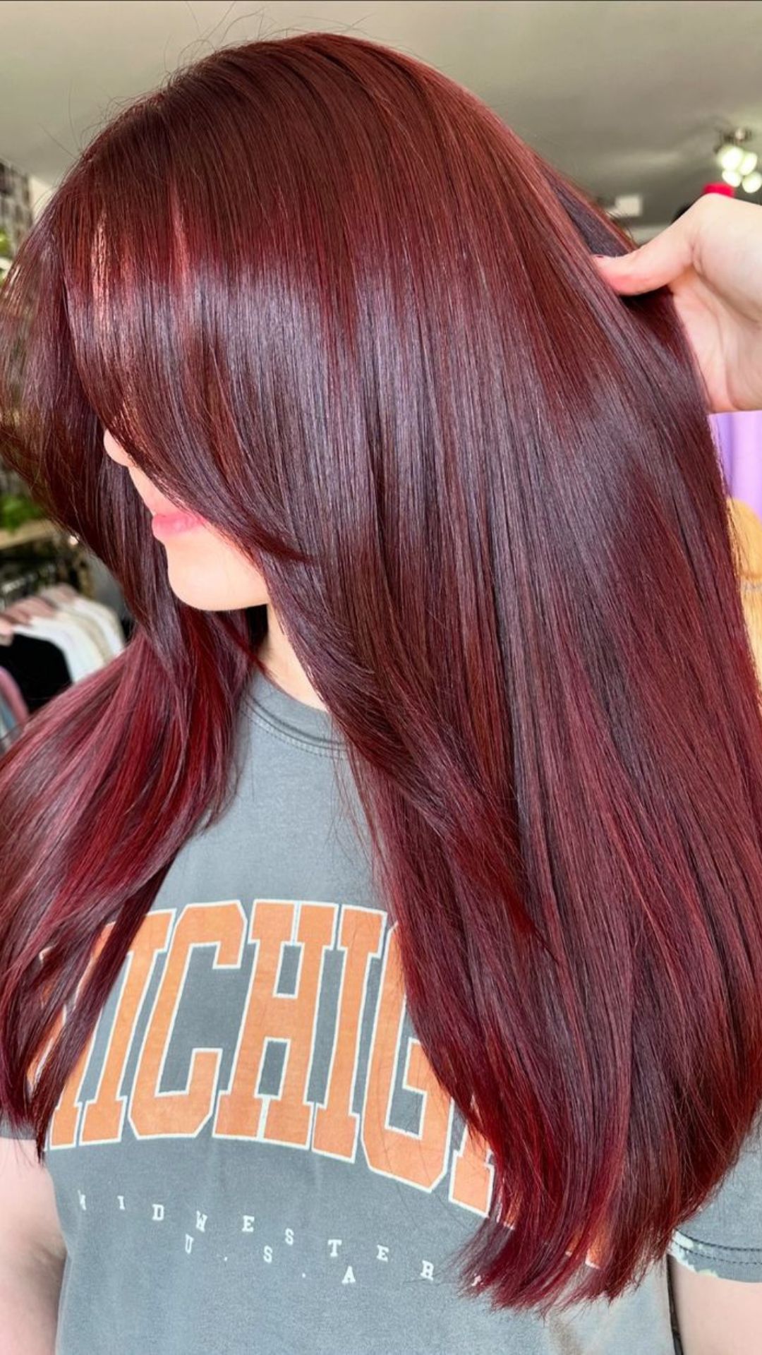 Woman modeling Cherry Cola hairstyle with long, straight reddish-brown hair, wearing a T-shirt.