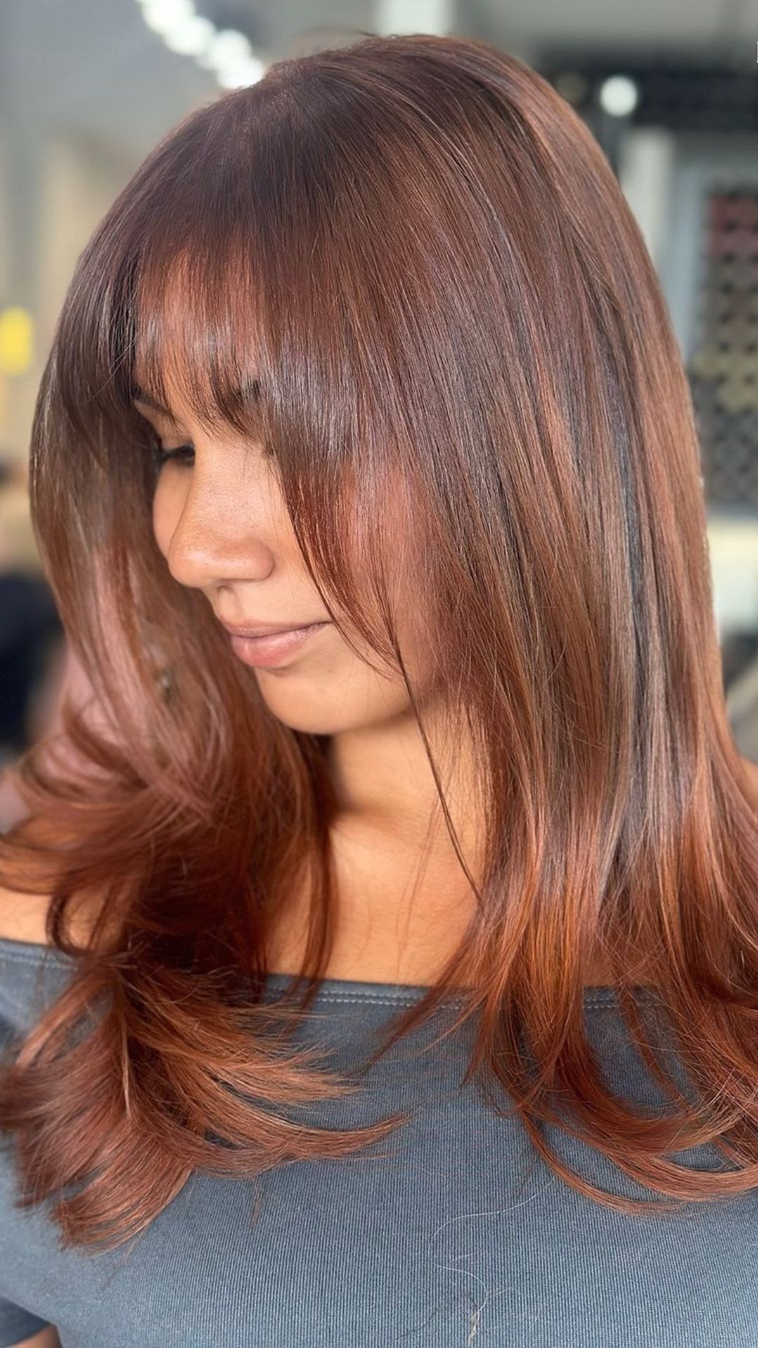 Close-up of a person with Cinnamon Copper hairstyle, featuring long, wavy hair with soft layers and subtle bangs.