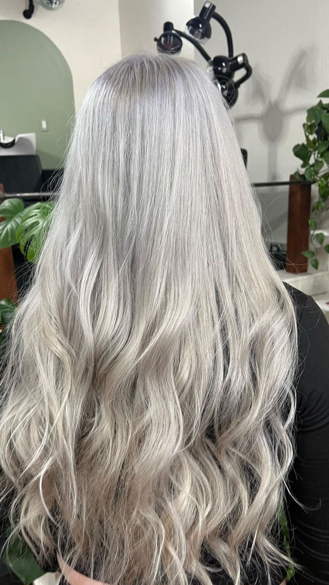 Person modeling Icy Platinum Blonde hairstyle with long, wavy hair, viewed from the back in a salon setting.