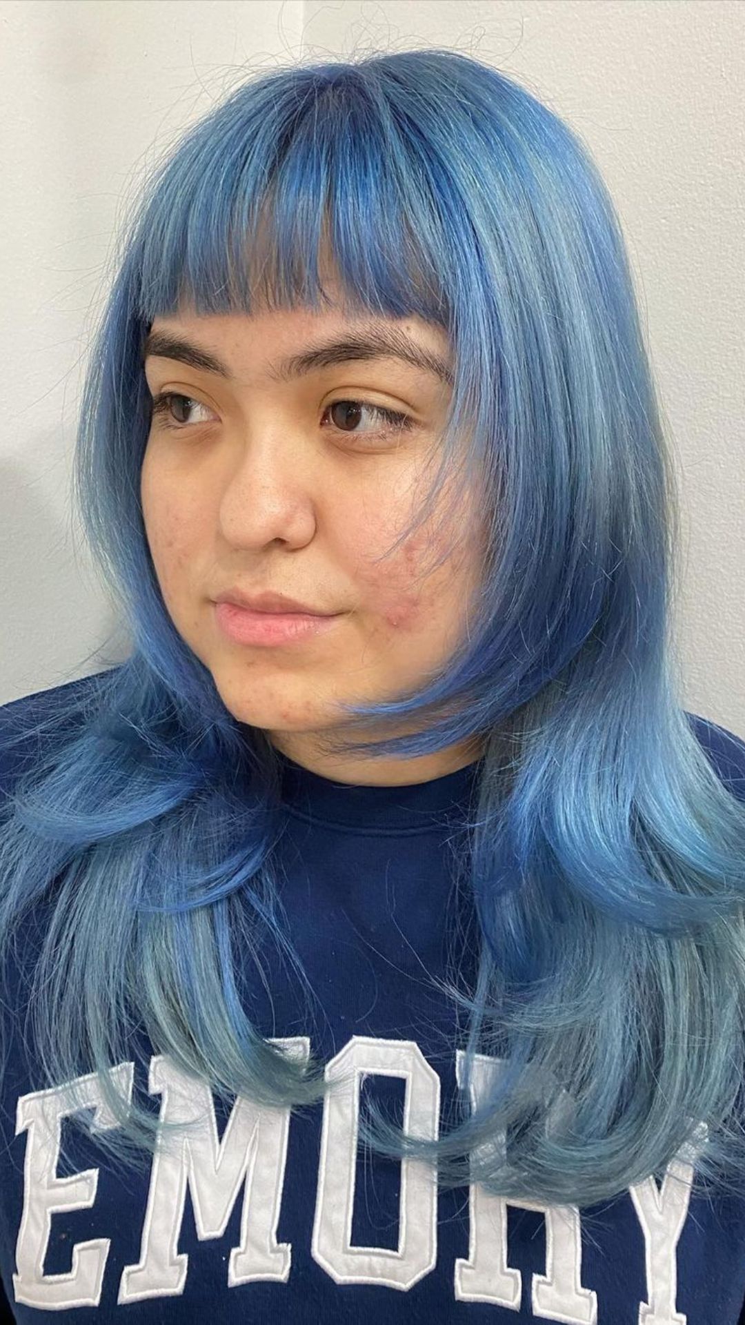 Person with straight, Pastel Blue hair and bangs, wearing a navy blue Emory shirt, looking away from the camera.