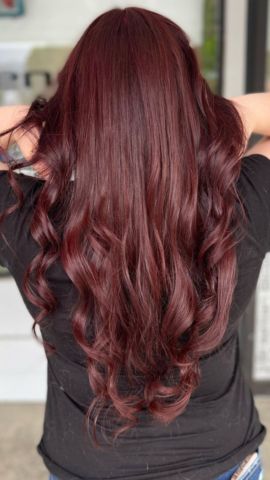 Back view of a person with long, wavy hair in a soft red color, wearing a black shirt.