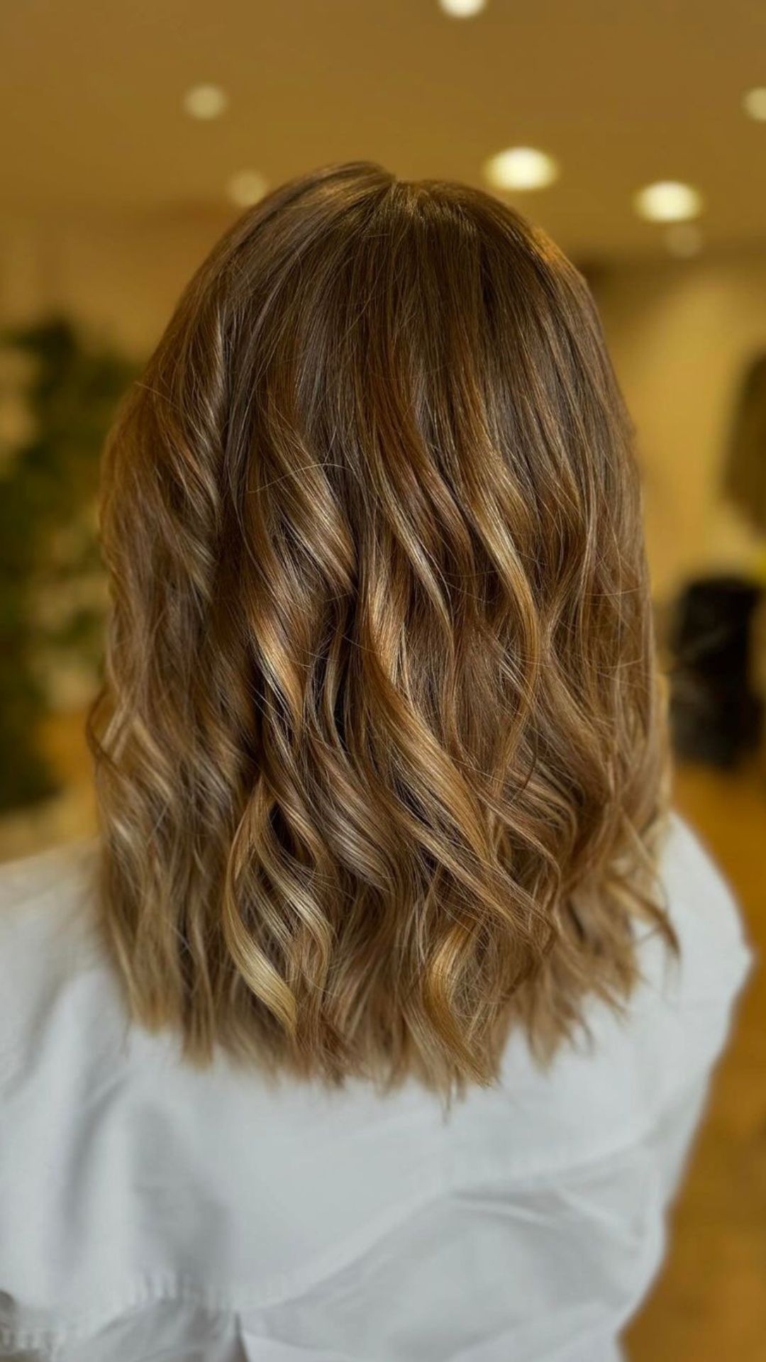 Woman with shoulder-length, wavy hair showcasing a subtle ombré hairstyle in a salon setting.