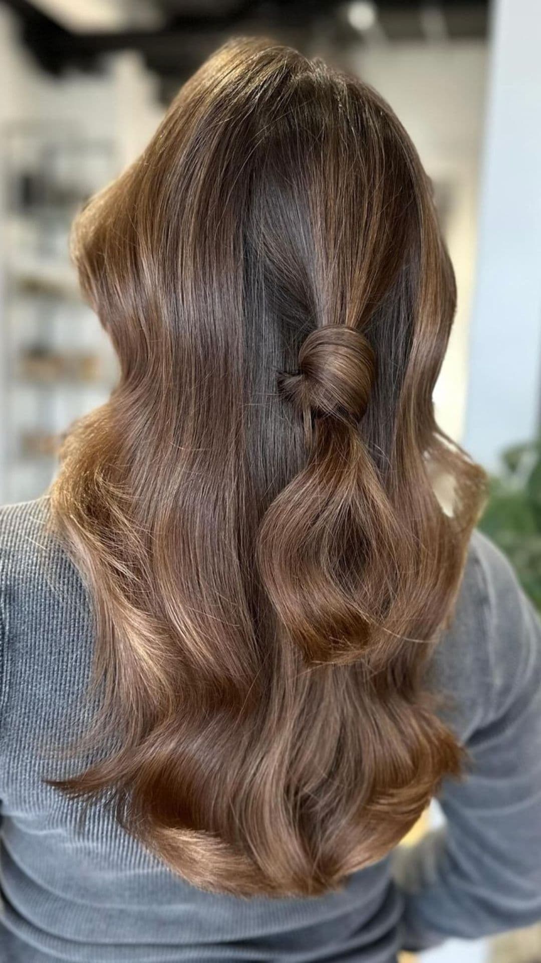 Back view of person with Amber Brown hairstyle, featuring long, wavy hair styled in a half-up knot.