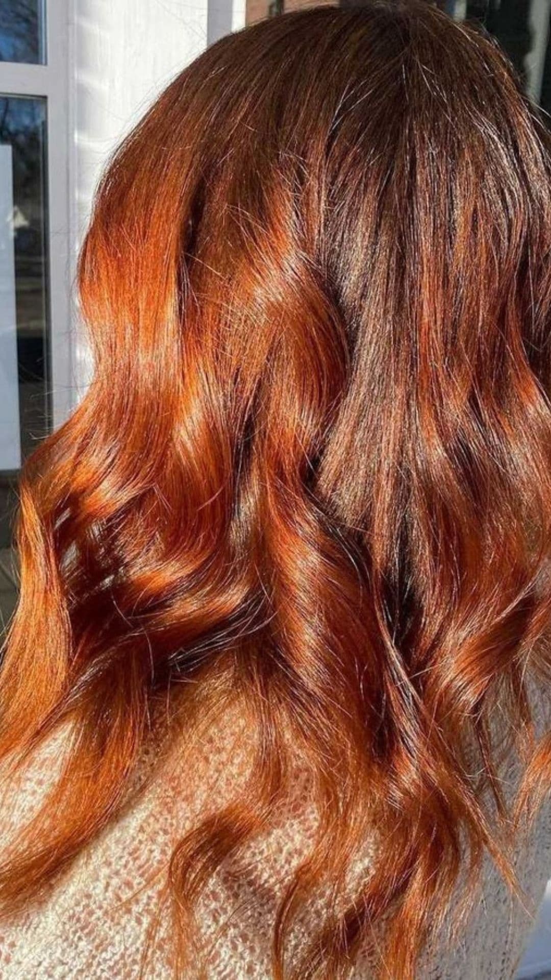 Close-up of a person modeling Sunlit Copper hairstyle with wavy, shiny hair.