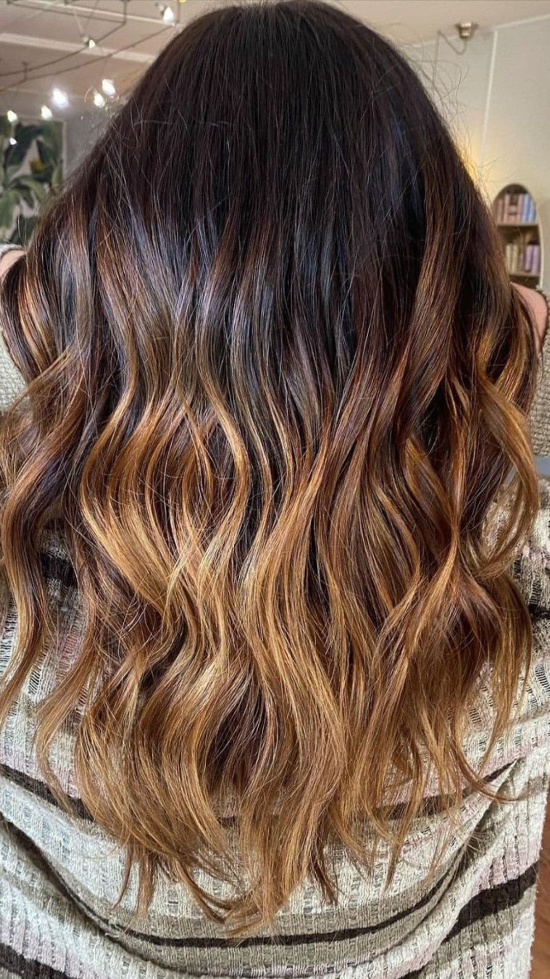 Woman showcasing the Toffee Melt hairstyle with wavy, dark brown hair transitioning to warm, caramel tones.