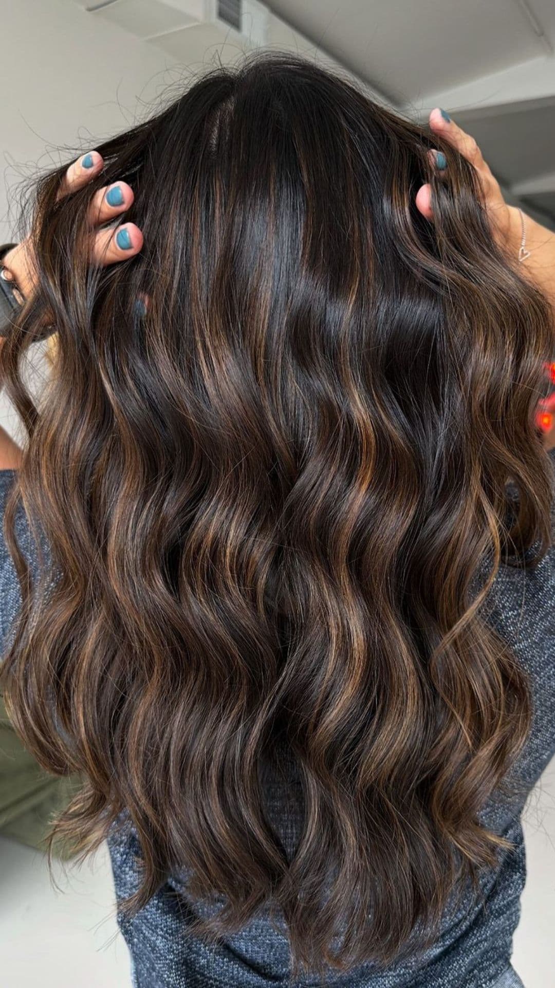 A person showcases their Warm Honey Brunette hairstyle, with long, wavy hair and subtle highlights.