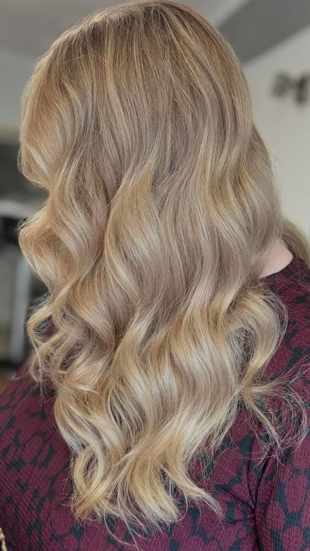 Woman with Balayage Blonde Curls hairstyle, wearing a dark patterned top, facing away.