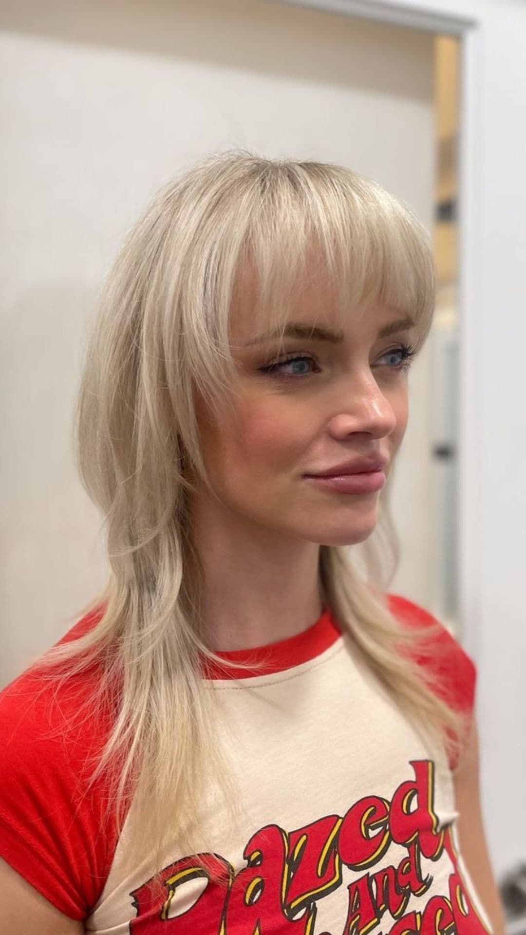 A person with a blonde shag hairstyle wearing a red and white shirt, facing right.