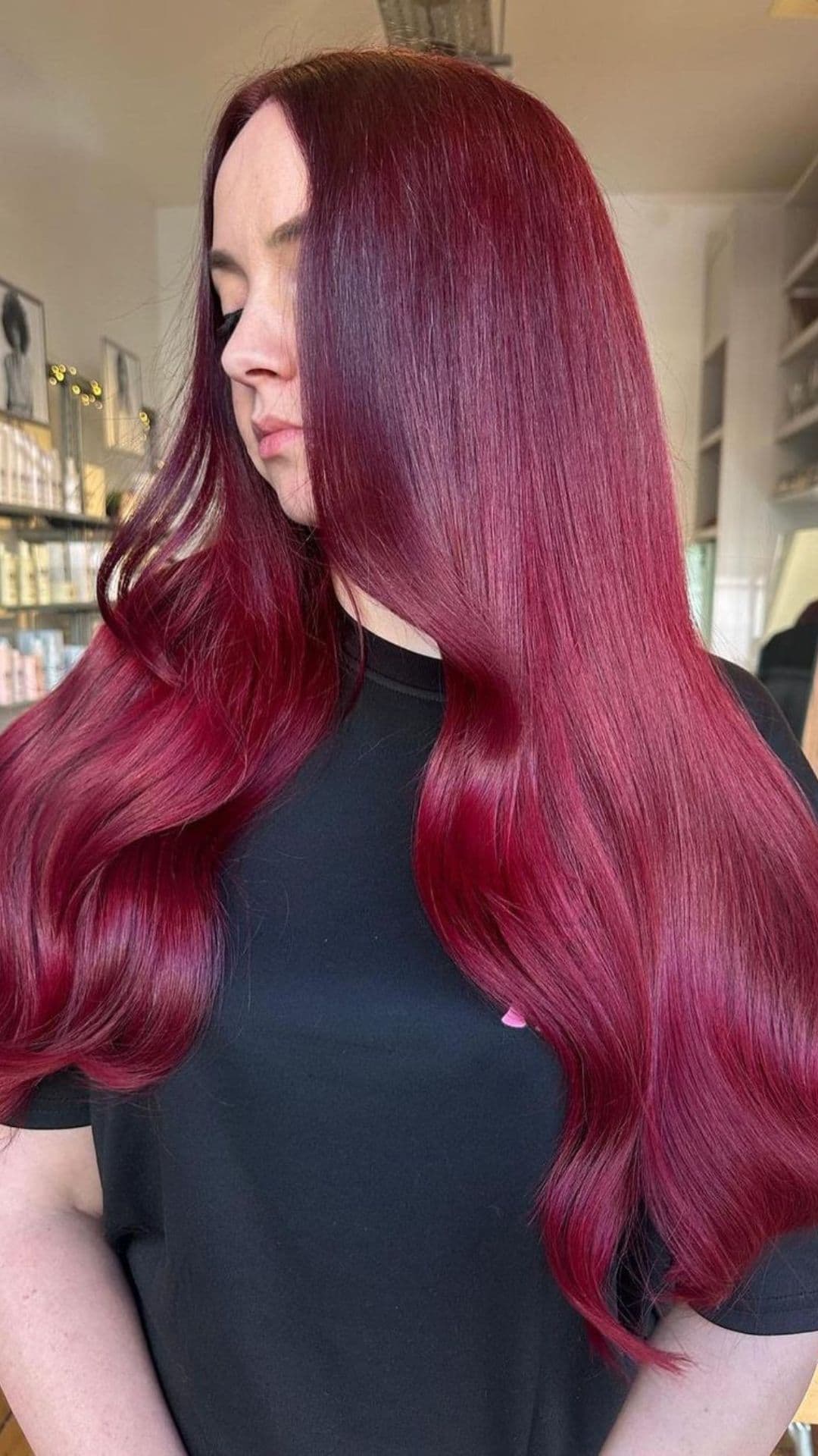 Woman with long, smooth Cherry Cola hairstyle, wearing a black t-shirt, standing in a salon.