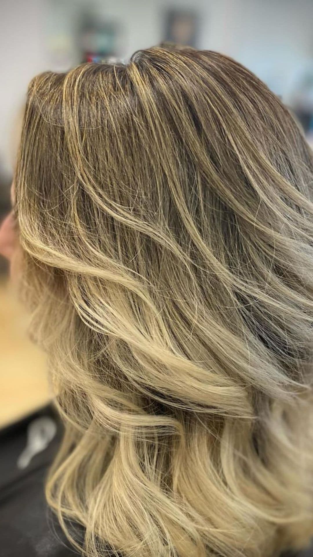 A person showcasing a Blended Blonde Highlights hairstyle with naturally flowing waves in a salon setting.