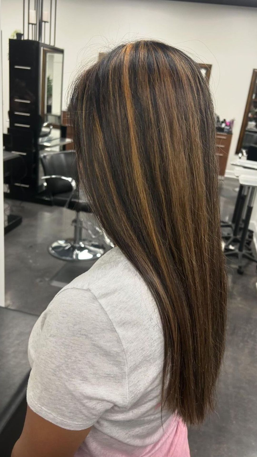 A person with long, straight hair showcasing a Caramel Lowlights hairstyle in a salon setting.