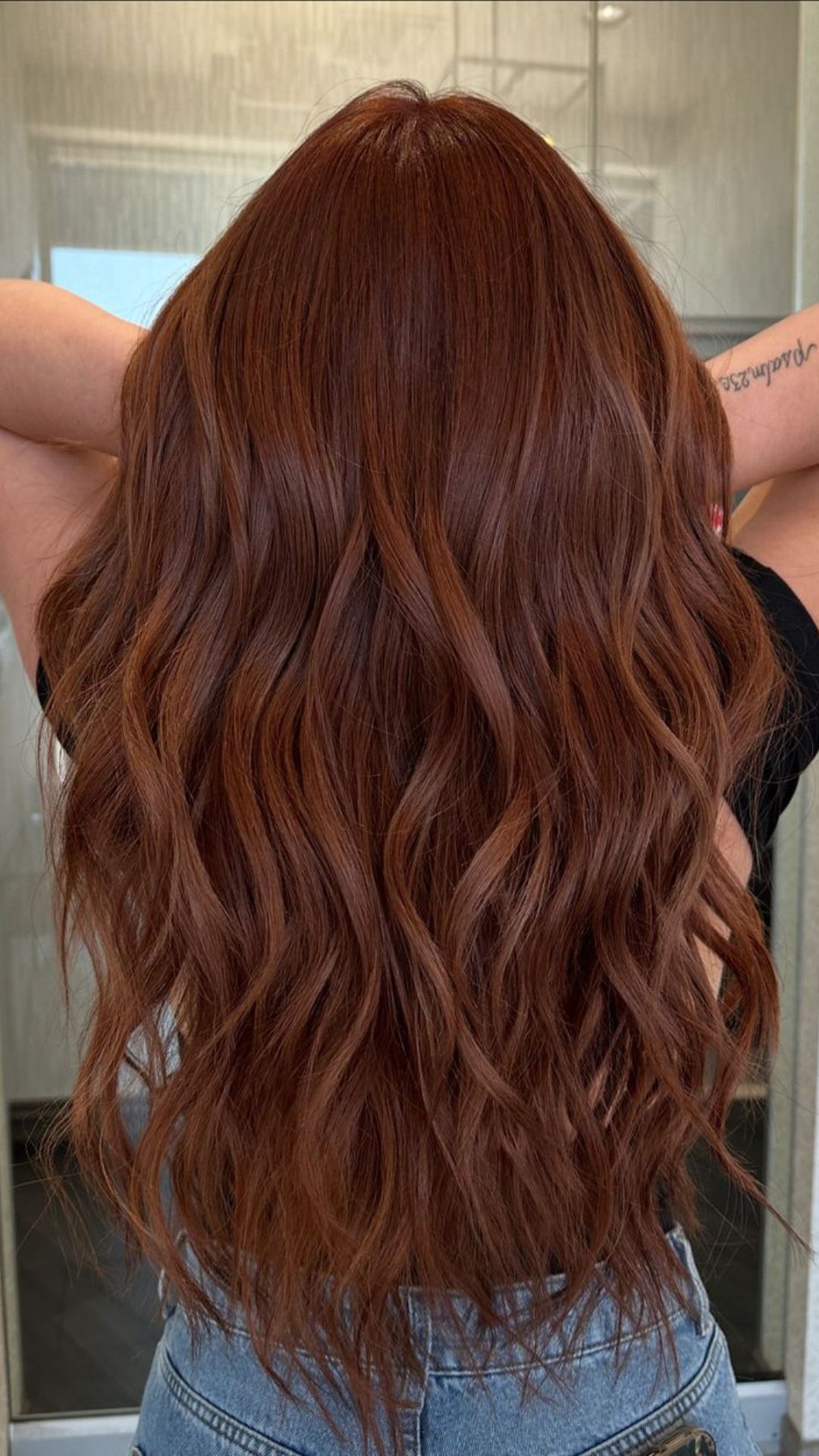 Back view of a person modeling with long, wavy copper-colored hair, showcasing a vibrant copper hairstyle.