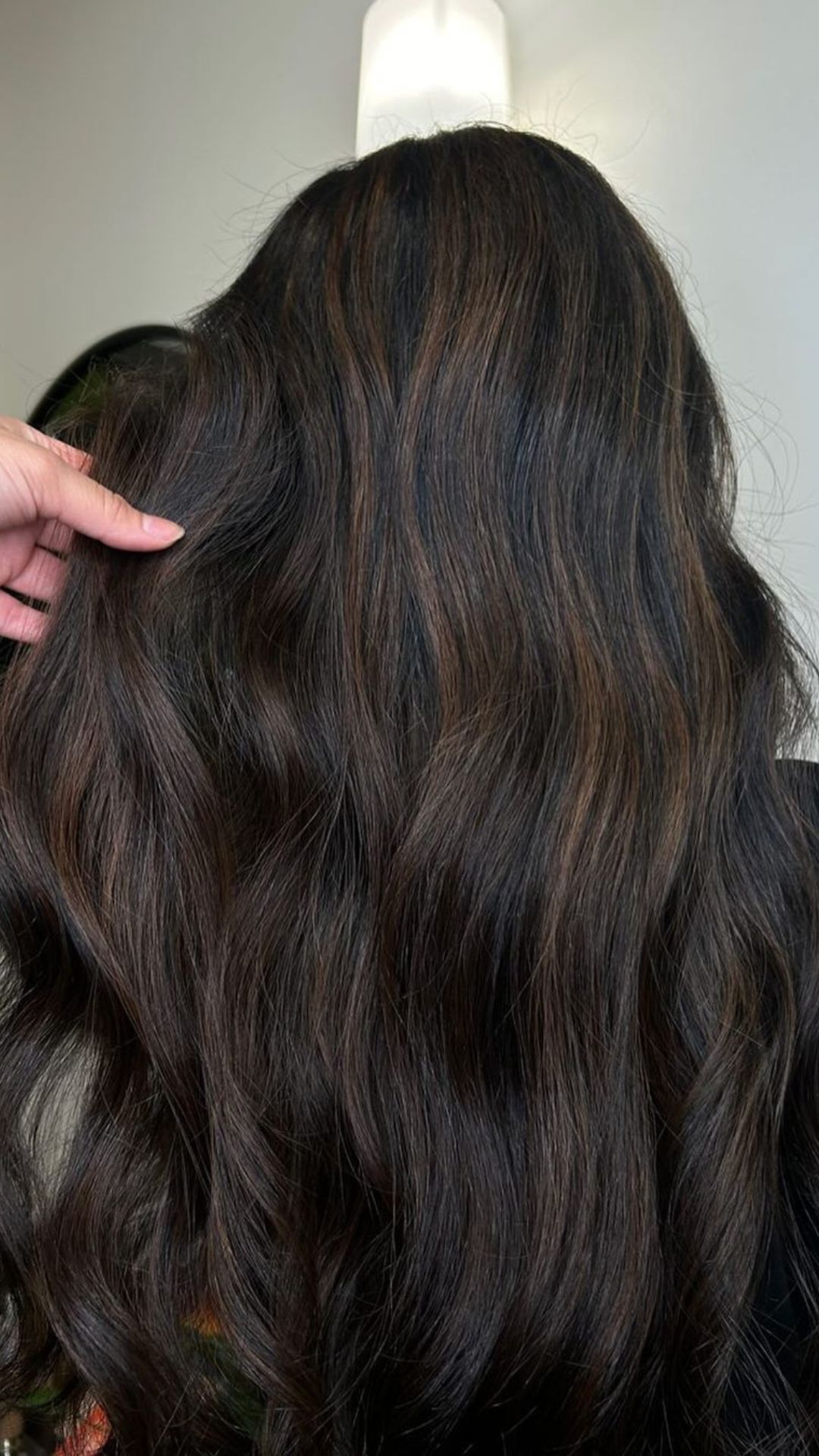 A person showcasing long, wavy hair with an Espresso hairstyle, featuring rich, dark brown tones and soft highlights.