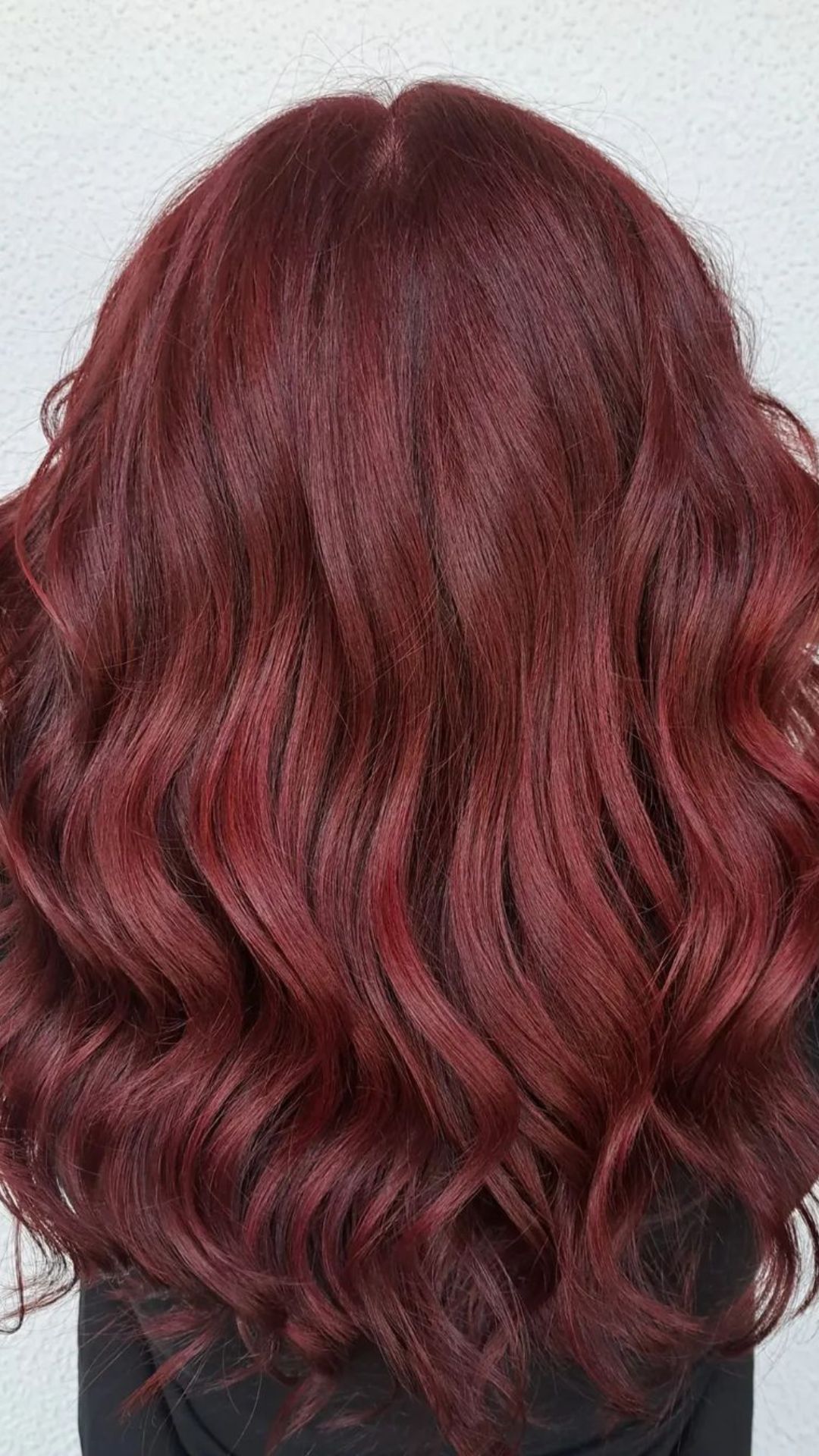 A person showcasing a Mulled Wine hairstyle with long, wavy, rich red hair.