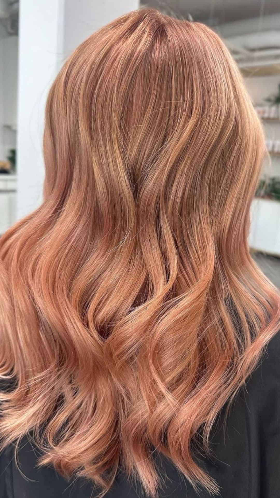 A person showcasing a Rose Gold hairstyle with flowing, wavy hair in a salon setting.