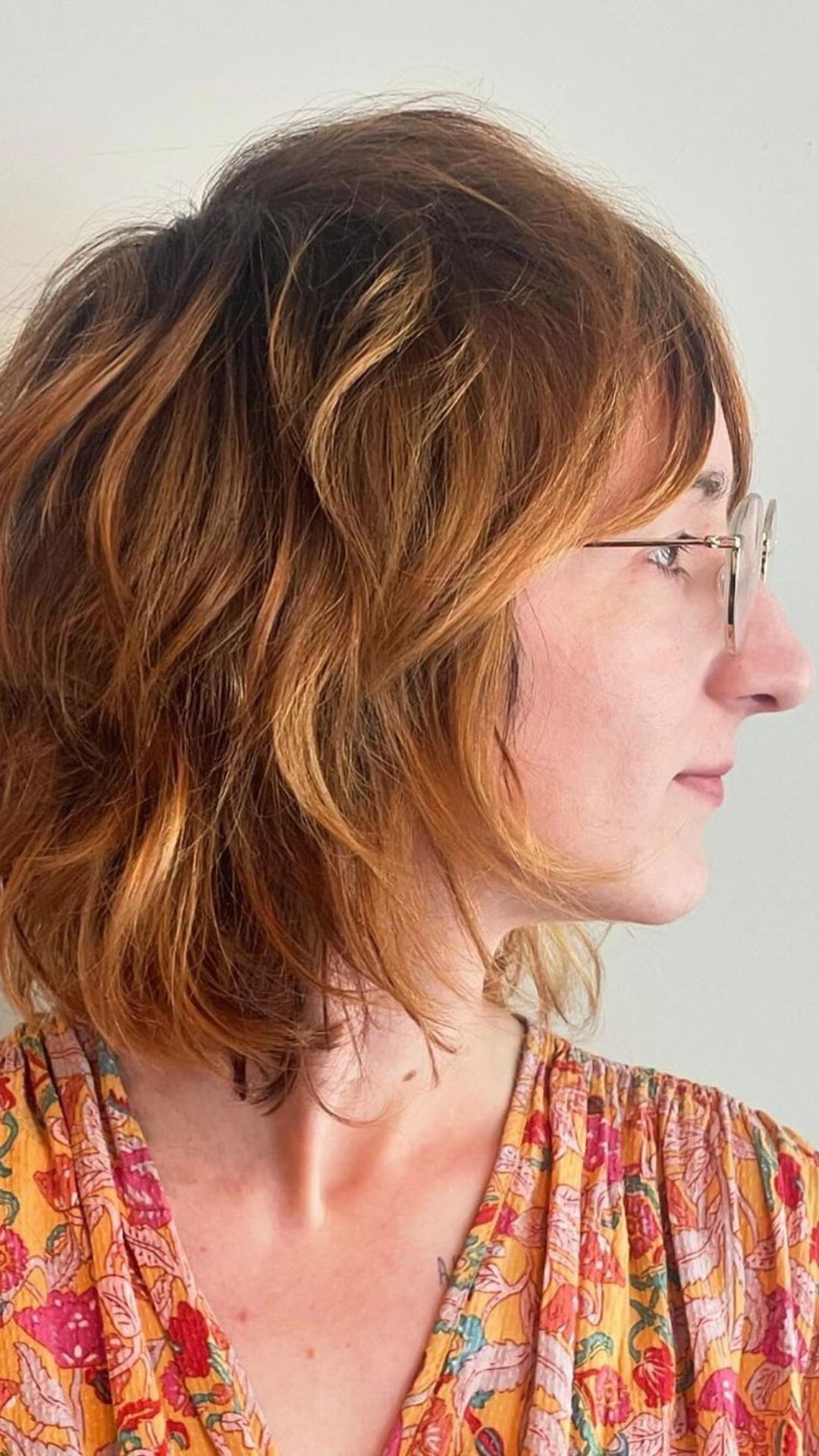 A person with glasses showing a strawberry blonde hairstyle, wearing a colorful floral top.