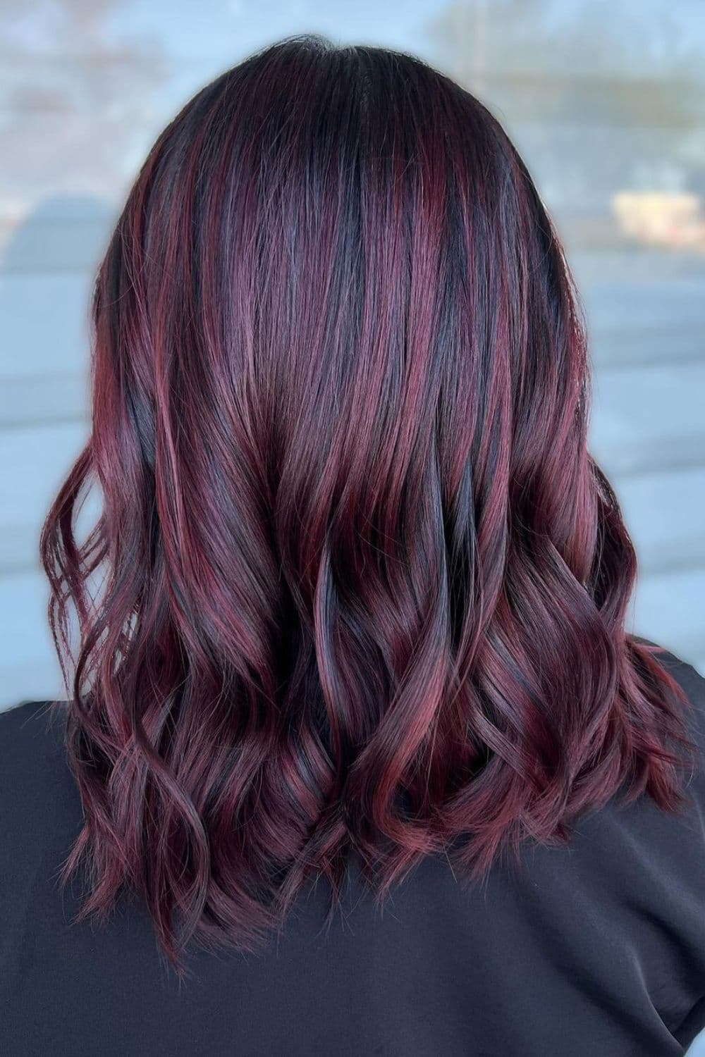 A woman with long bob cut with burgundy balayage.