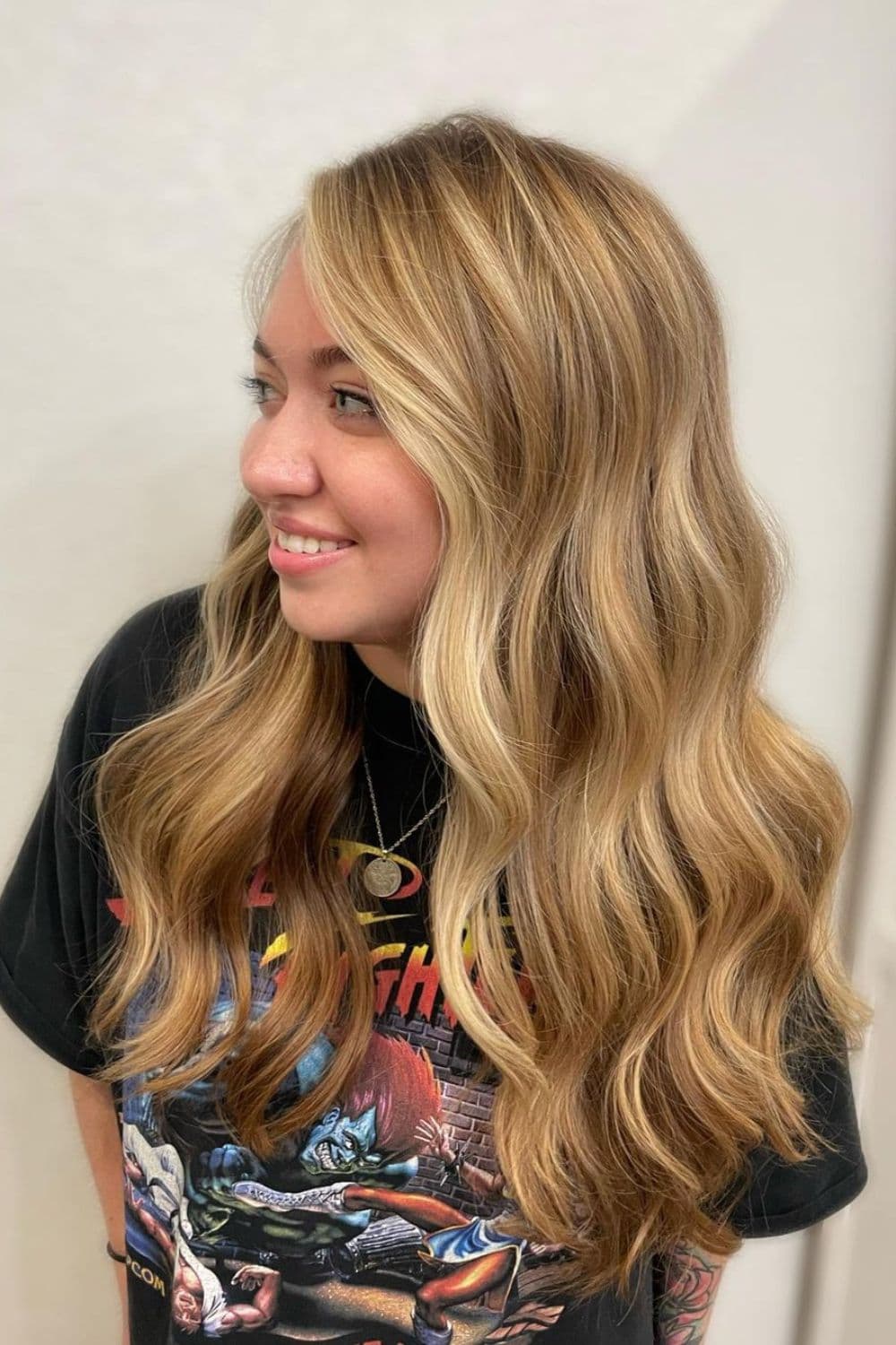 A woman with long wavy dirty blonde hair with blonde money pieces.