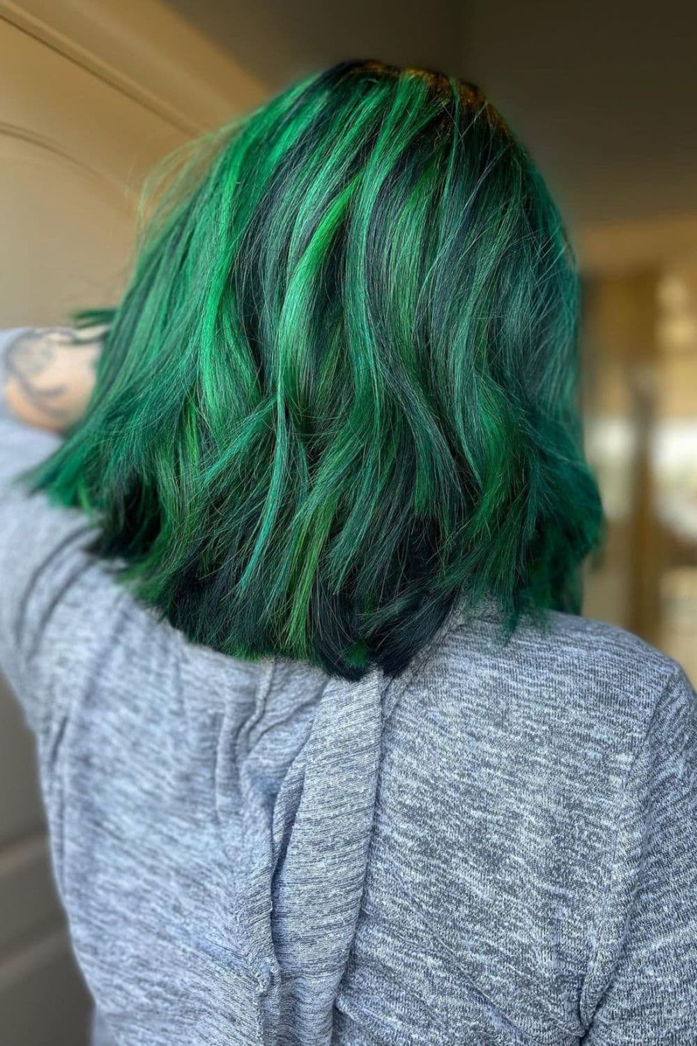 A woman with a long bob cut with emerald green balayage.