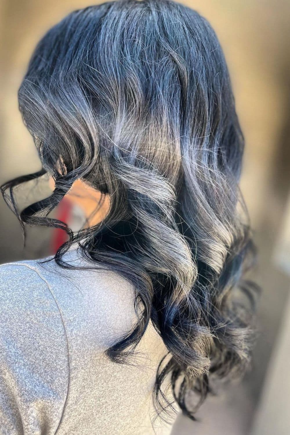 A woman with medium-length frosty dark blue black hair with big curls.