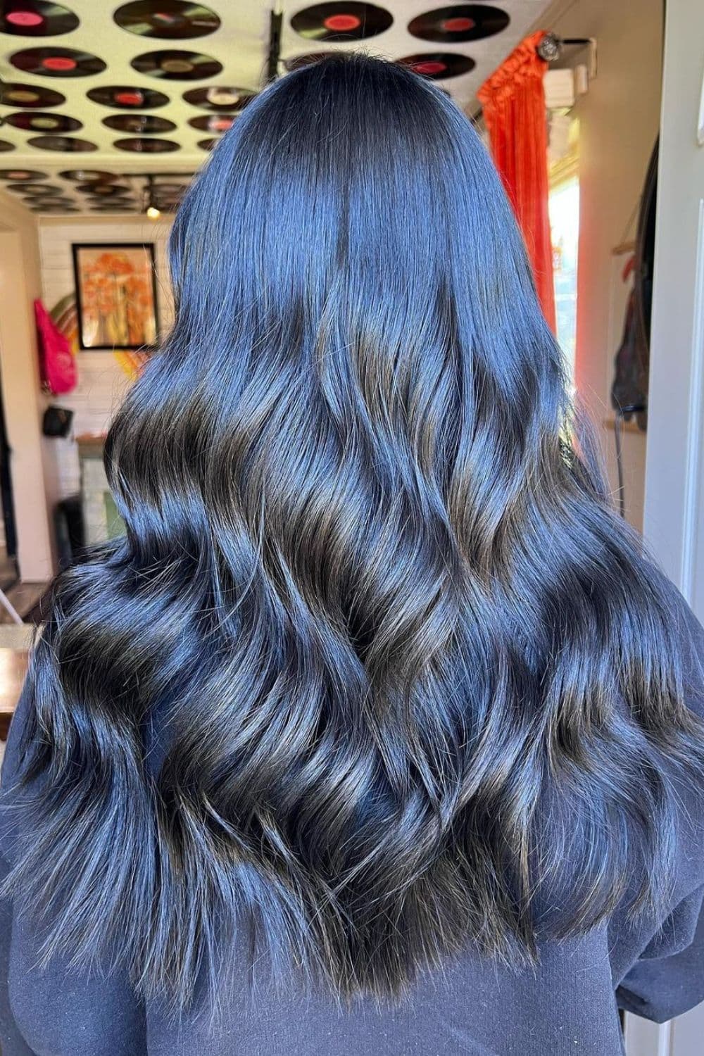 A woman with long metallic blue black hair with beach waves.